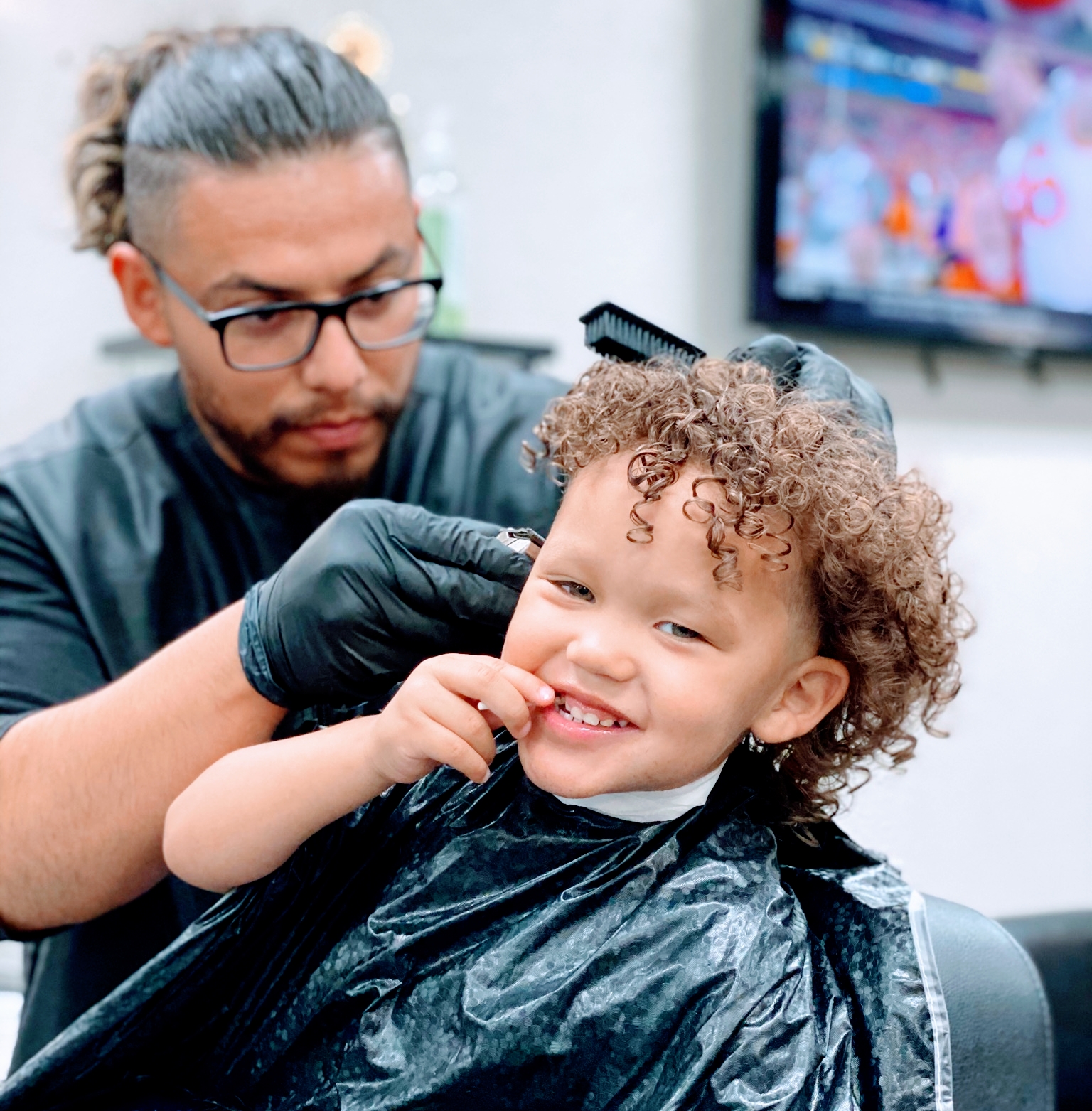 Barber cutting a smiling young child's curly hair in the shop